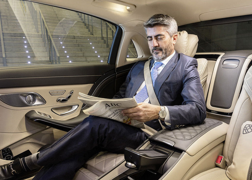 Man in a suit reading a newspaper in a luxury car.