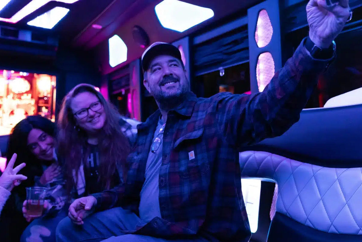 People inside a limousine with a man taking a selfie, illuminated by blue and purple lights.